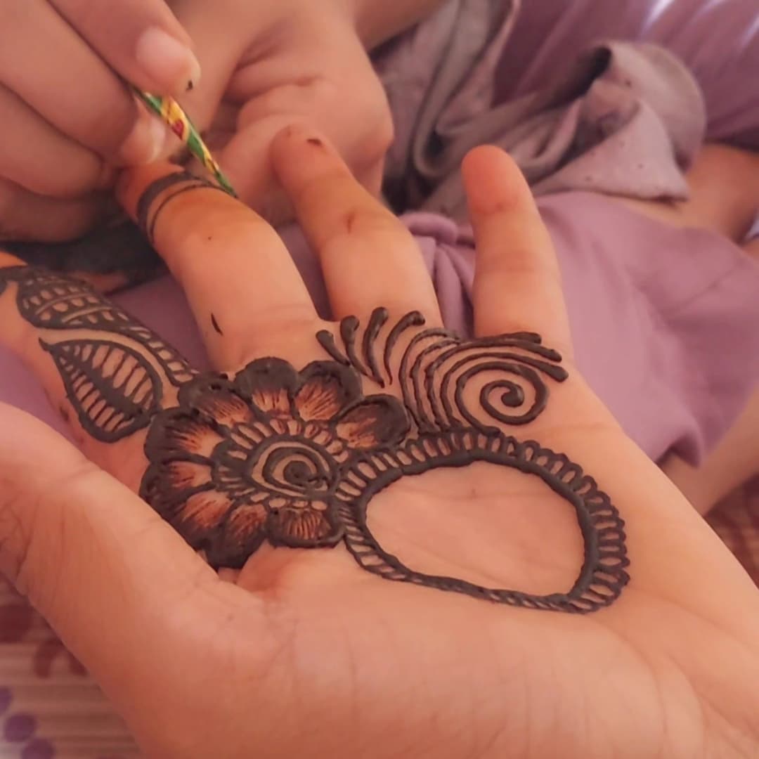 A floral henna mandala being applied to a hand the night before a celebration.