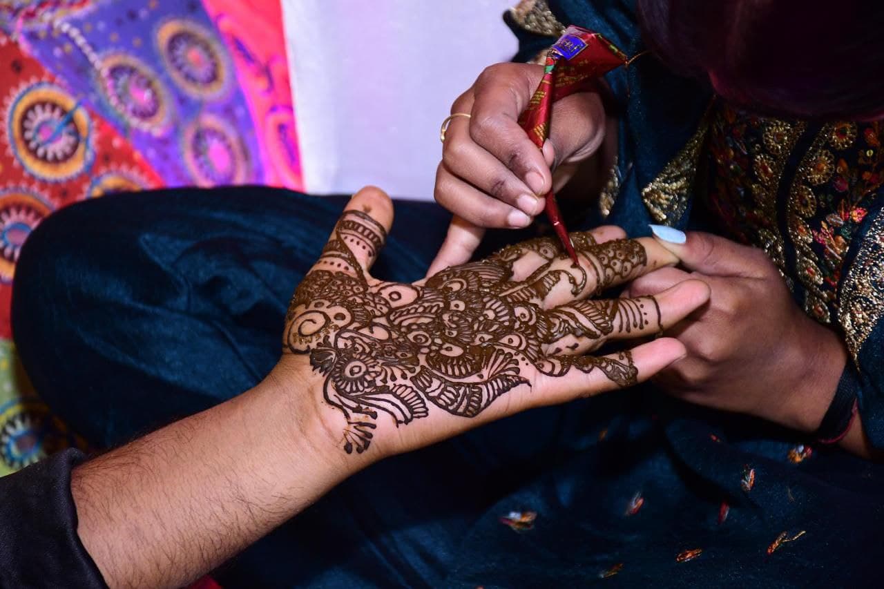 Intricate henna being applied to a bride's hands at a celebration.